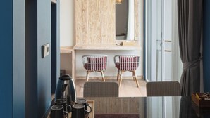 Una habitación de hotel moderna con una mesa de comedor de vidrio, dos sillas, una cafetera y un candelabro.