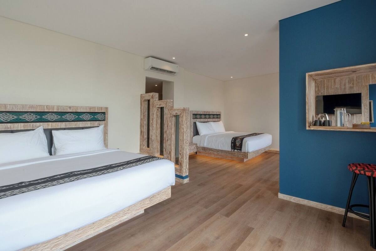 Ein Hotelzimmer mit zwei Betten, einem spiegelnden Holzrahmen, Holzboden und einer Klimaanlage.
