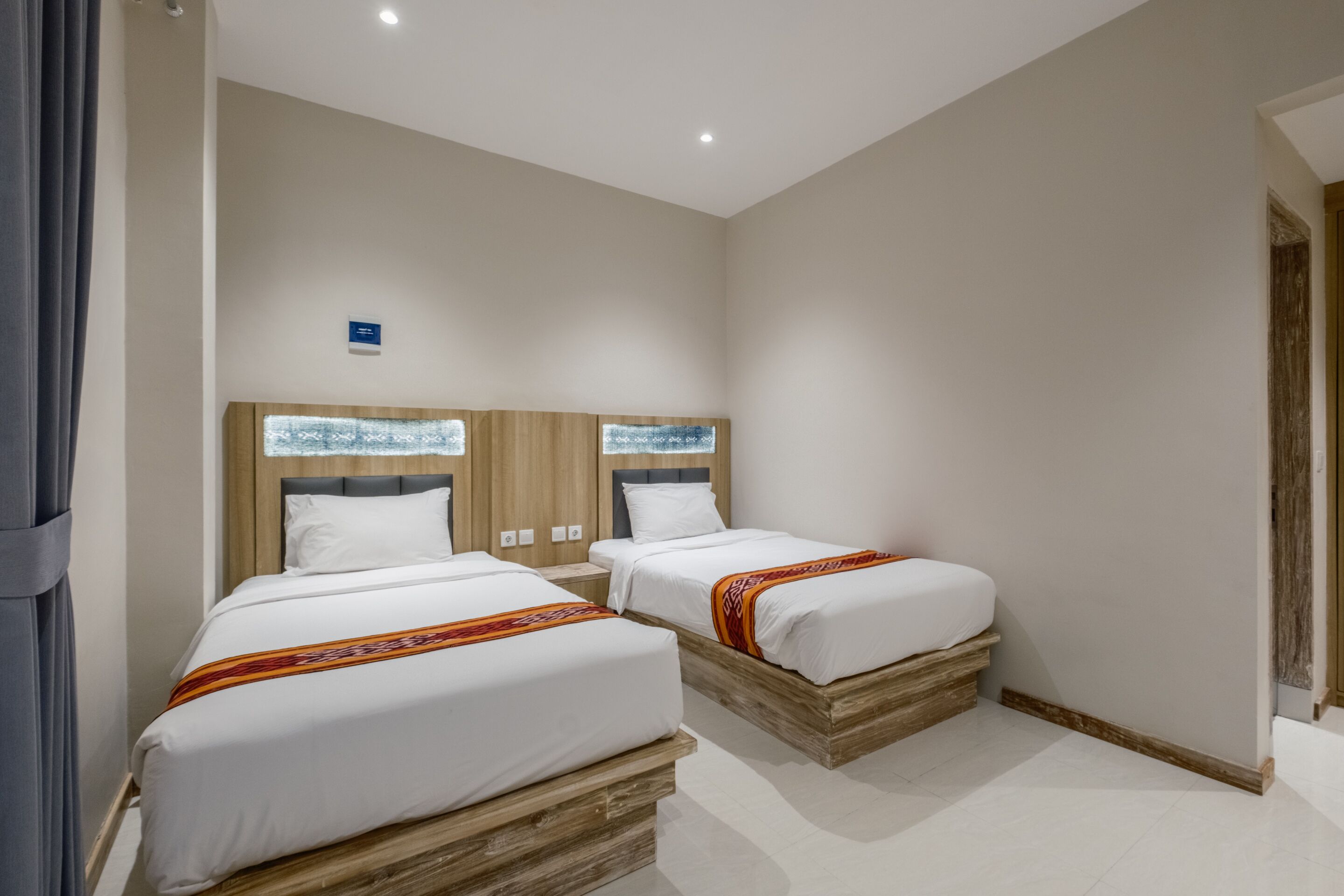 A hotel room with two beds, wooden headboards, white bedding, and a small bedside table.