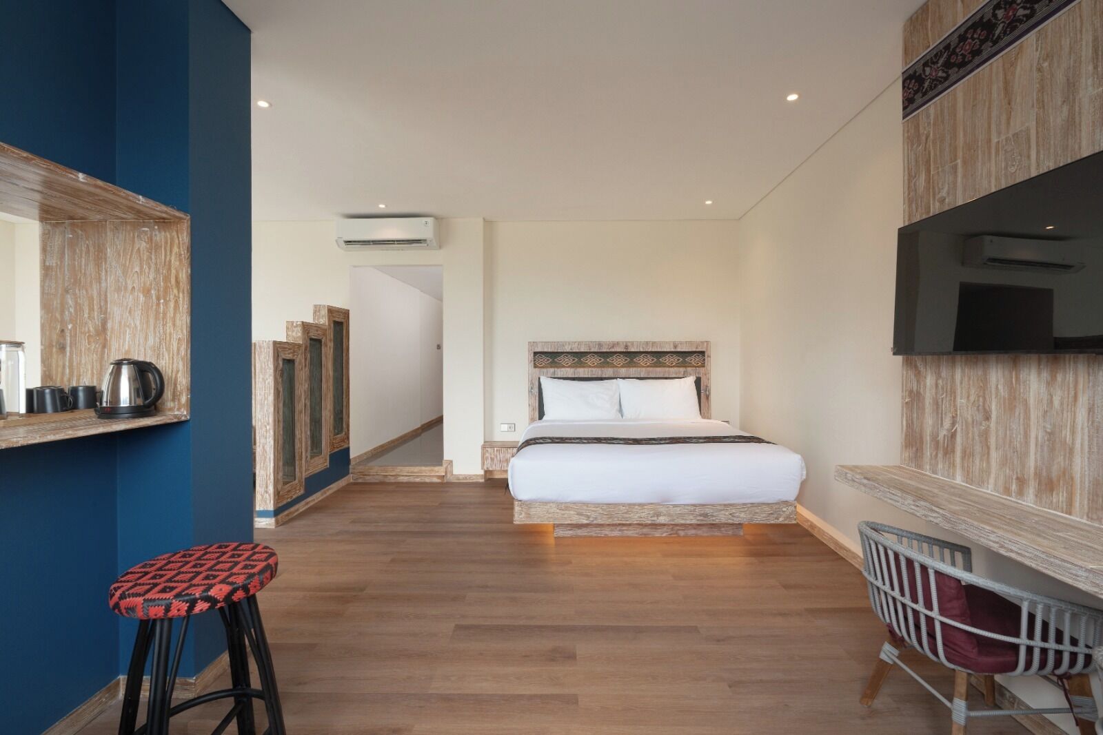 A hotel room with a bed, a TV, a coffee maker, and a stool.