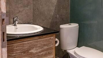 A bathroom with a white sink, wooden vanity, a toilet, and a mirror.
