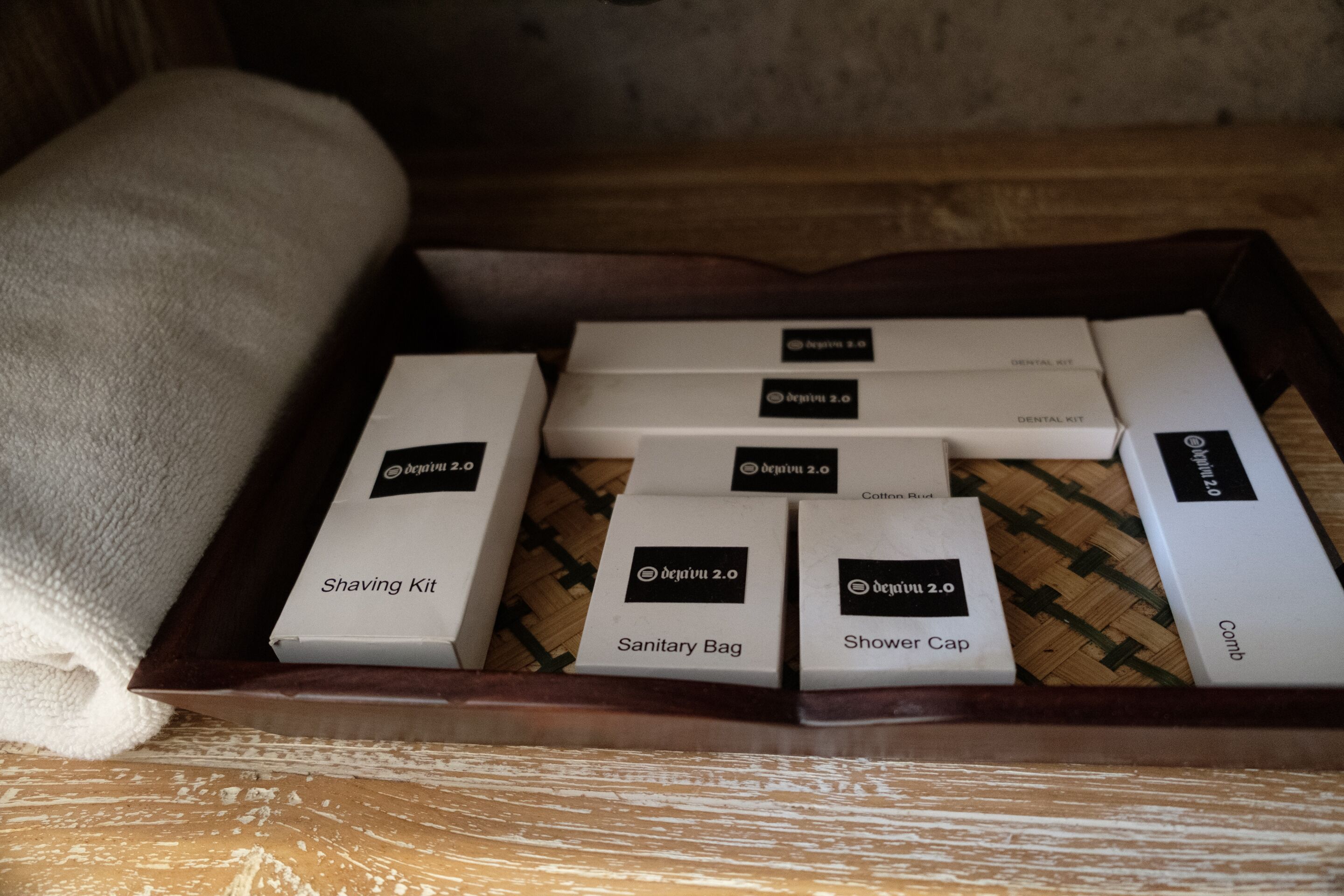 A wooden tray with several white boxes labeled with 'Shaving Kit,' 'Sanitary Bag,' 'Shower Cap,' and 'Comb.'
