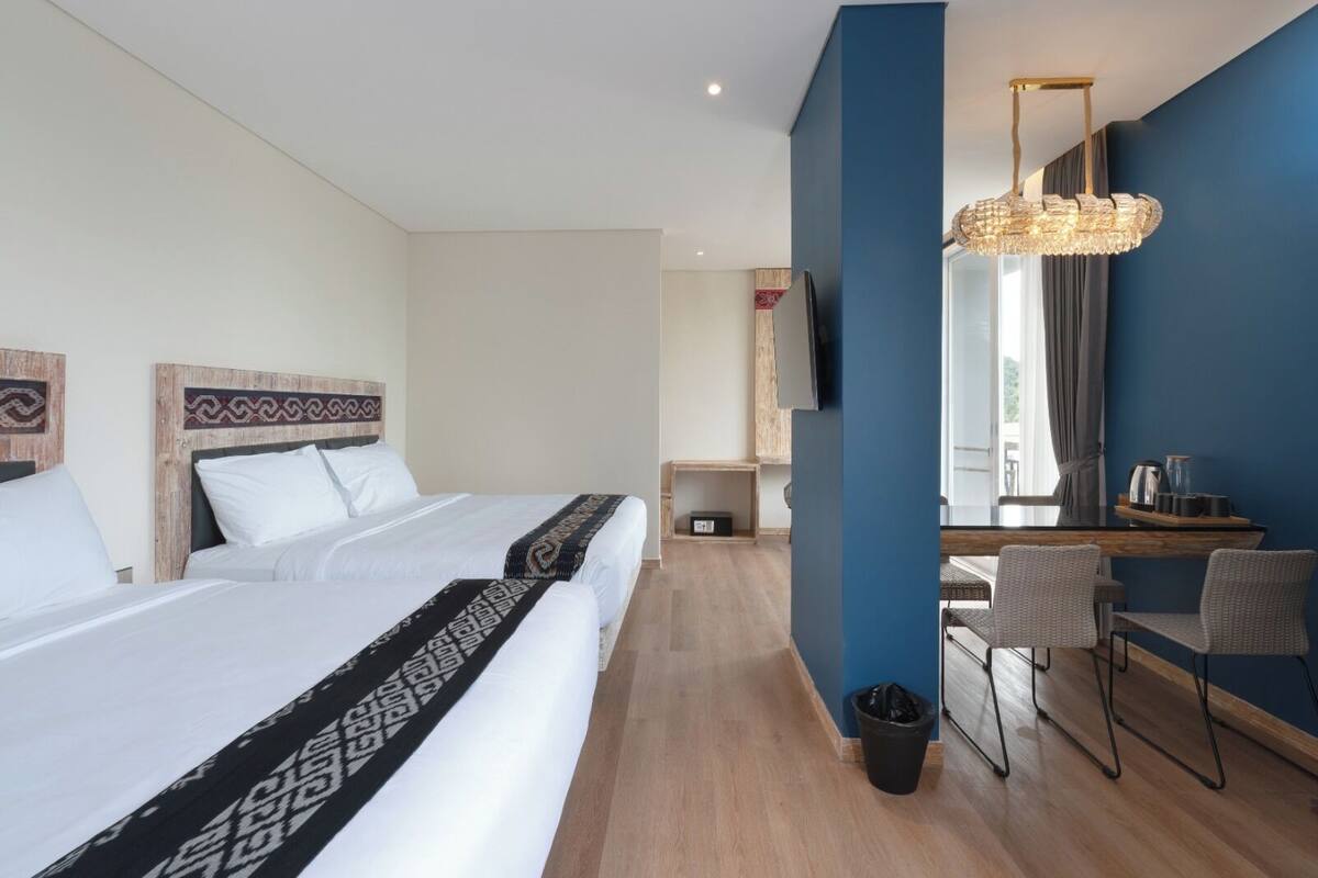Ein Hotelzimmer mit zwei Betten, einem Schreibtisch mit Stühlen, einem Mülleimer und einer Deckenleuchte.