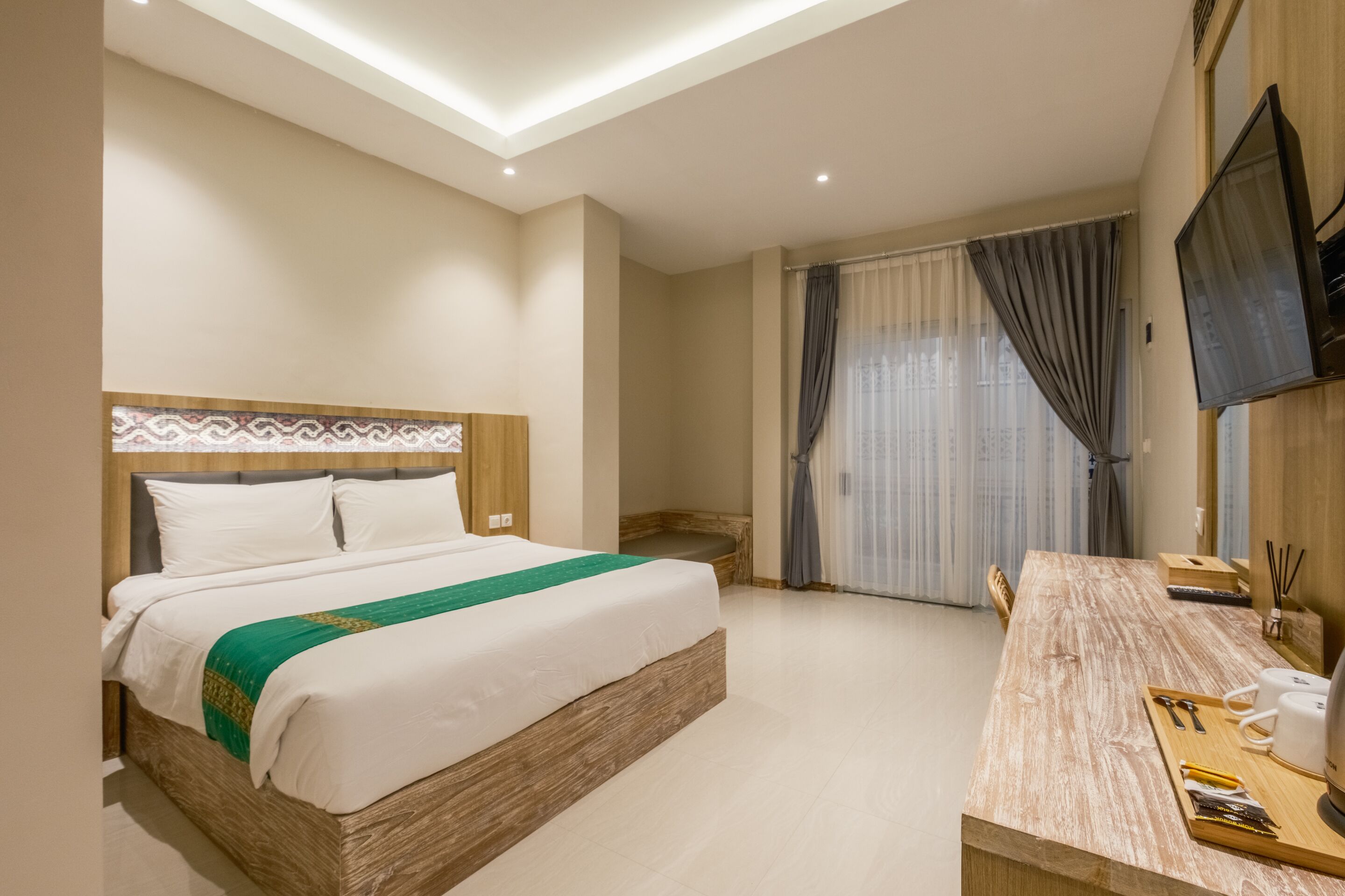 Ein Hotelzimmer mit einem Bett, einem Holztisch, einem Fernseher und einem Fenster mit Vorhängen.