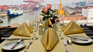 A table set for two with a view of a port and cranes in the background. - Grand Oriental Hotel (Colombo)