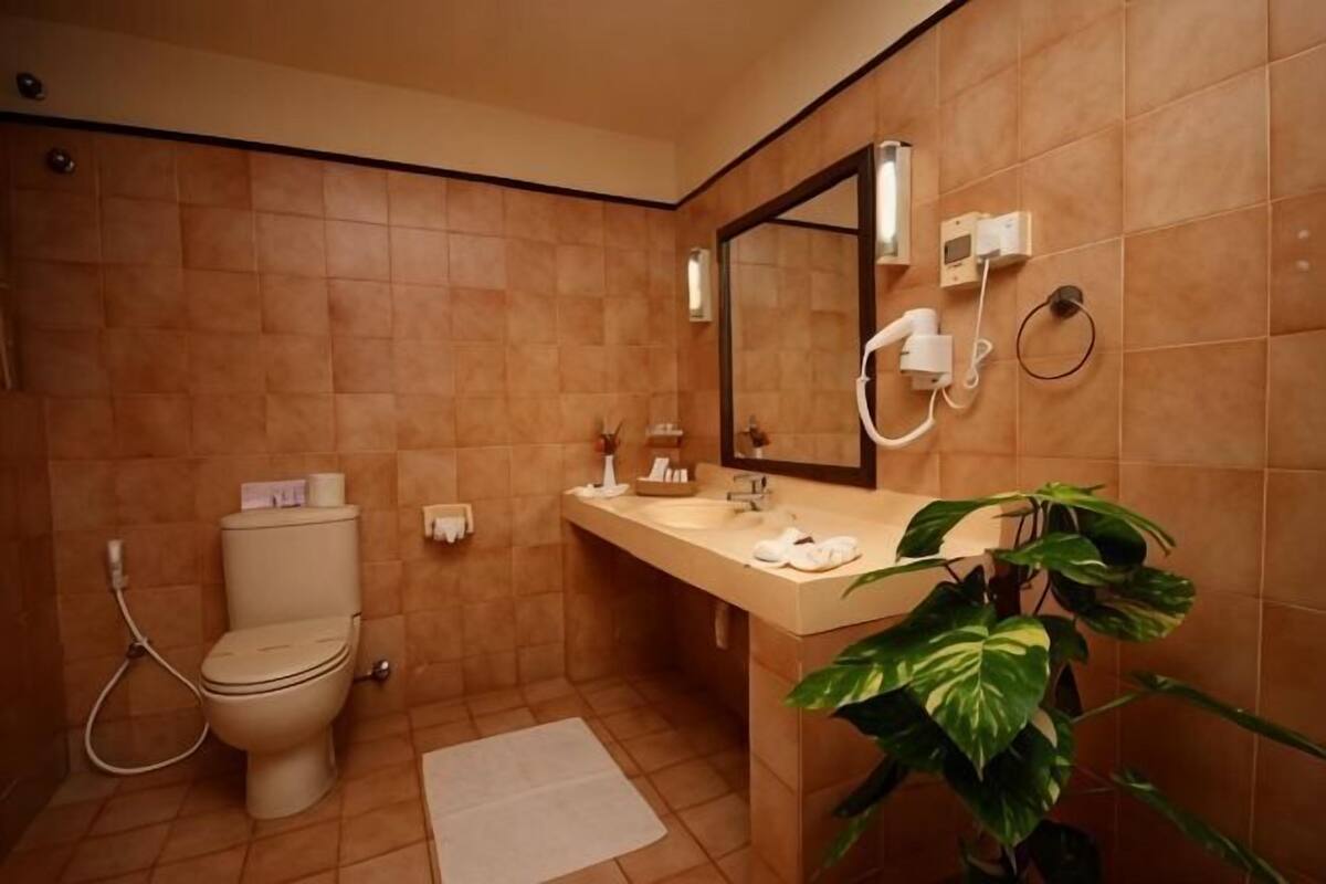A bathroom with a toilet, sink, mirror, and a plant.