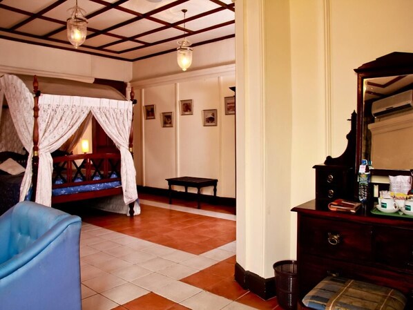 Una habitación con cama con dosel, un banco de madera, un aparador y un espejo.