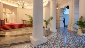 A grand lobby with white columns, a red carpeted staircase, and patterned flooring. - Grand Oriental Hotel (Colombo)