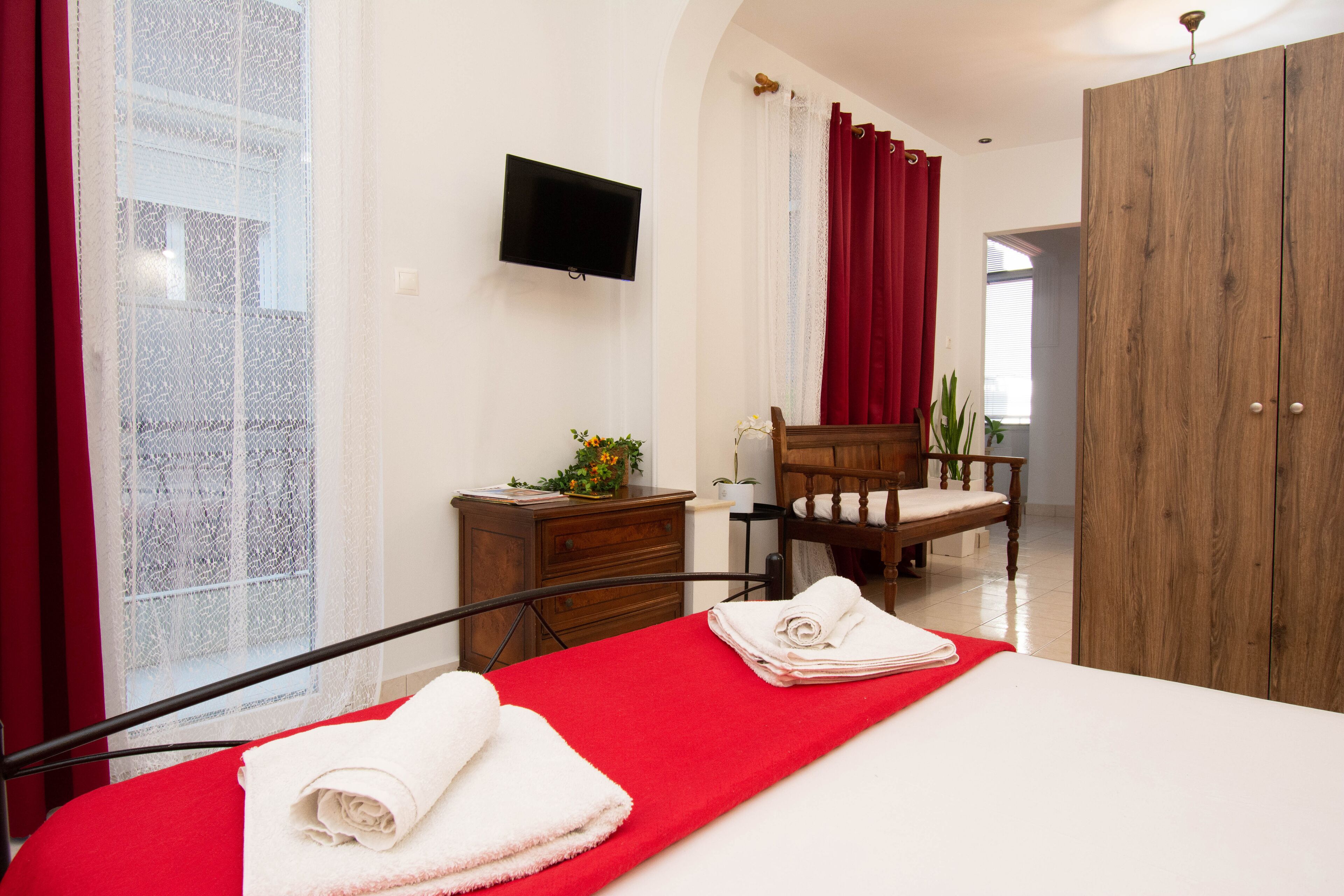 A hotel room with a bed, a wooden wardrobe, a television, a desk with a plant, and a chair.
