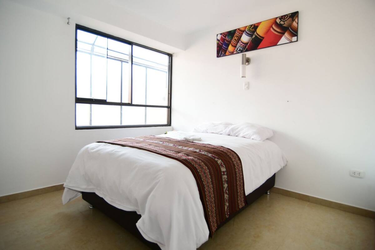 A bedroom with a bed, a window, and a wall-mounted painting.