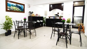 Un comedor moderno con sillas y mesas negras, una zona de cocina con armarios oscuros y un cuadro grande enmarcado en la pared.