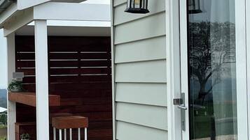 A covered outdoor area with a wooden deck, a white pergola, and a glass door with a sliding mechanism.