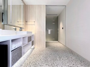Un baño moderno con tocador blanco, un espejo grande y zona de ducha.