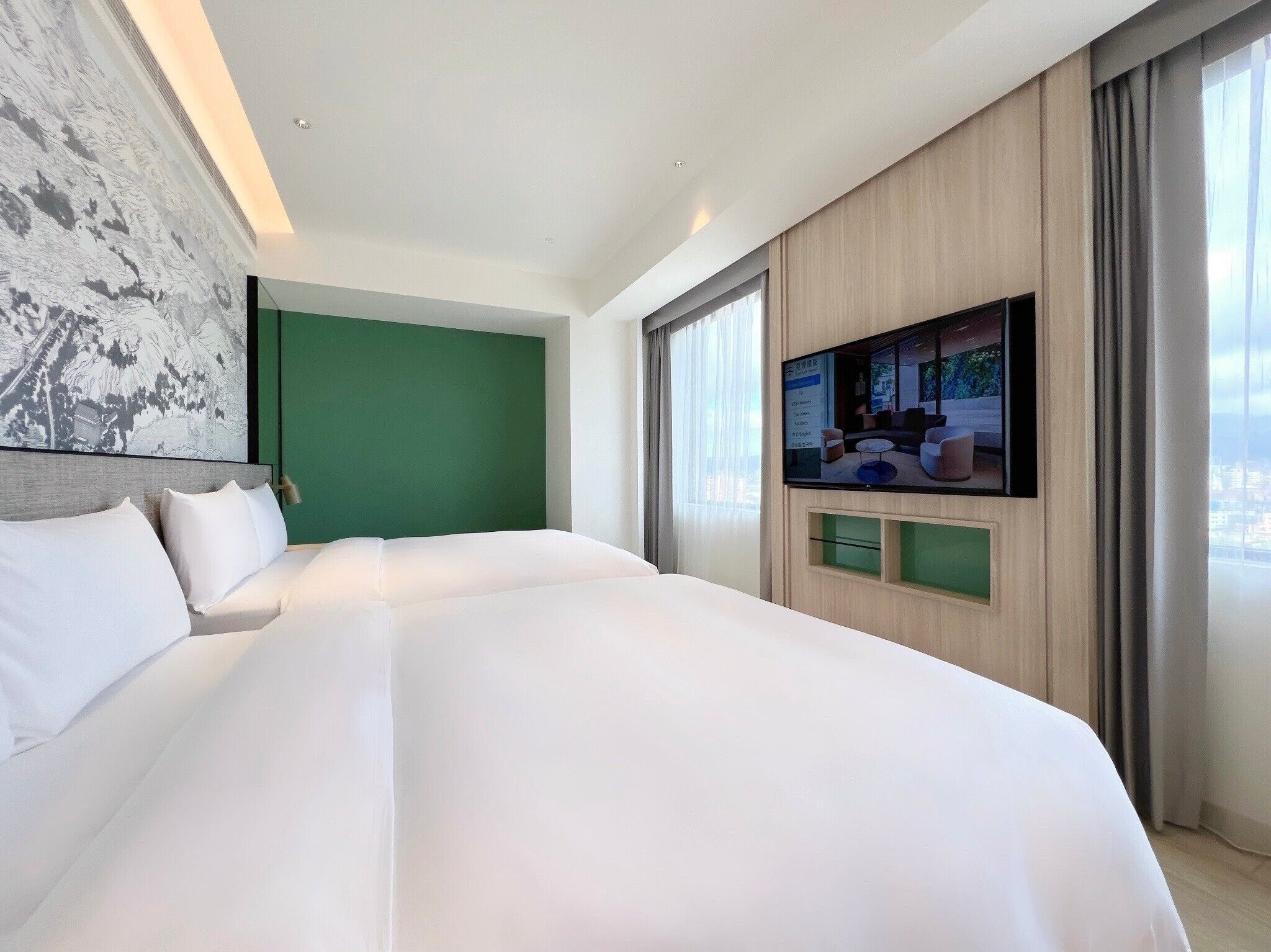 Una camera d'albergo moderna con un letto grande, una TV a schermo piatto fissata al muro e vista sulla città da ampie finestre.