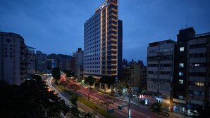 A high-rise hotel with multiple floors and balconies, surrounded by other buildings and busy streets at dusk. - Jiantan Boutech Hotel (Taipei)