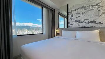 A hotel room with a large bed, a view of the cityscape, and a wall-mounted artwork.