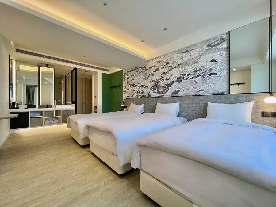 A hotel room with two beds, a large mirror, a wall with a detailed mural, and a small seating area with a table and chairs.
