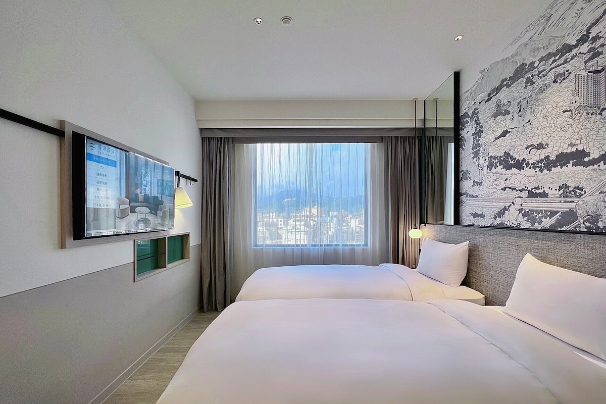 A hotel room with two beds, a TV, a city view, and a large artwork on the wall.