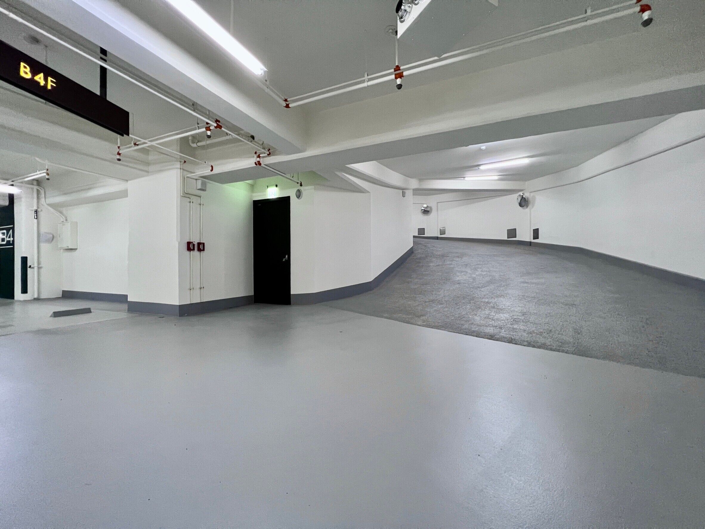 Ett stort, tomt parkeringsgarage med en ramp som leder till en dörr märkt B4F.