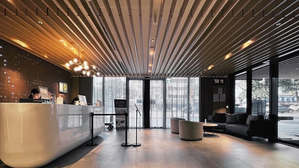A modern reception area with a curved reception desk, seating area with sofas, large windows, and a wooden ceiling. - Jiantan Boutech Hotel (Taipei)