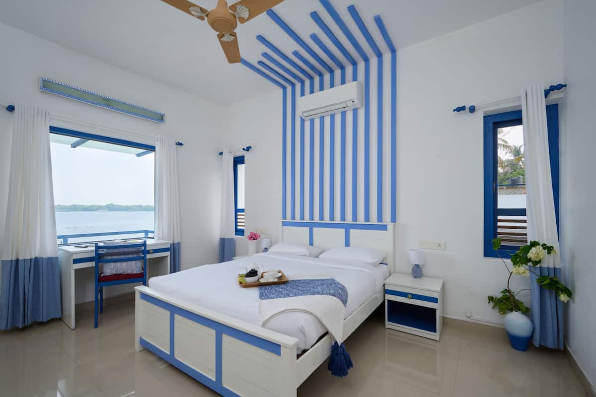 A bedroom with a bed, a desk, and a chair. There is a window with curtains, a ceiling fan, and an air conditioning unit.
