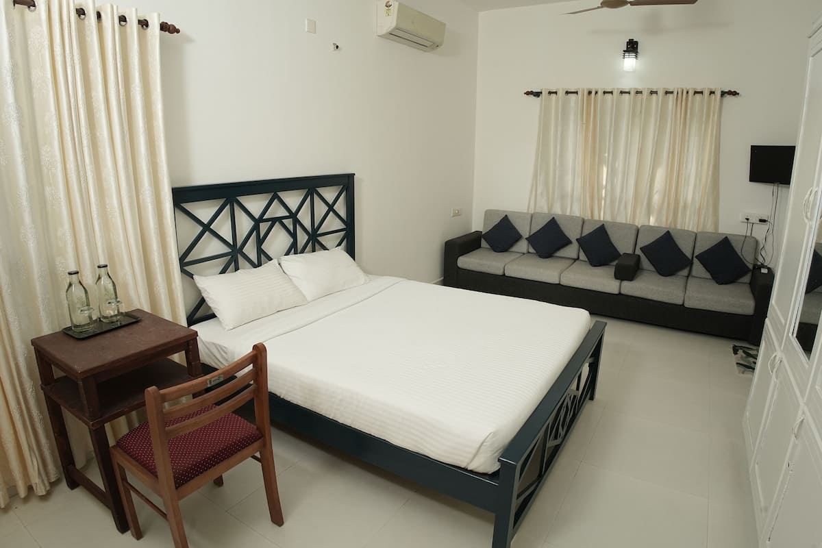 A bedroom with a bed, a sofa, a chair, a small table, and a TV.