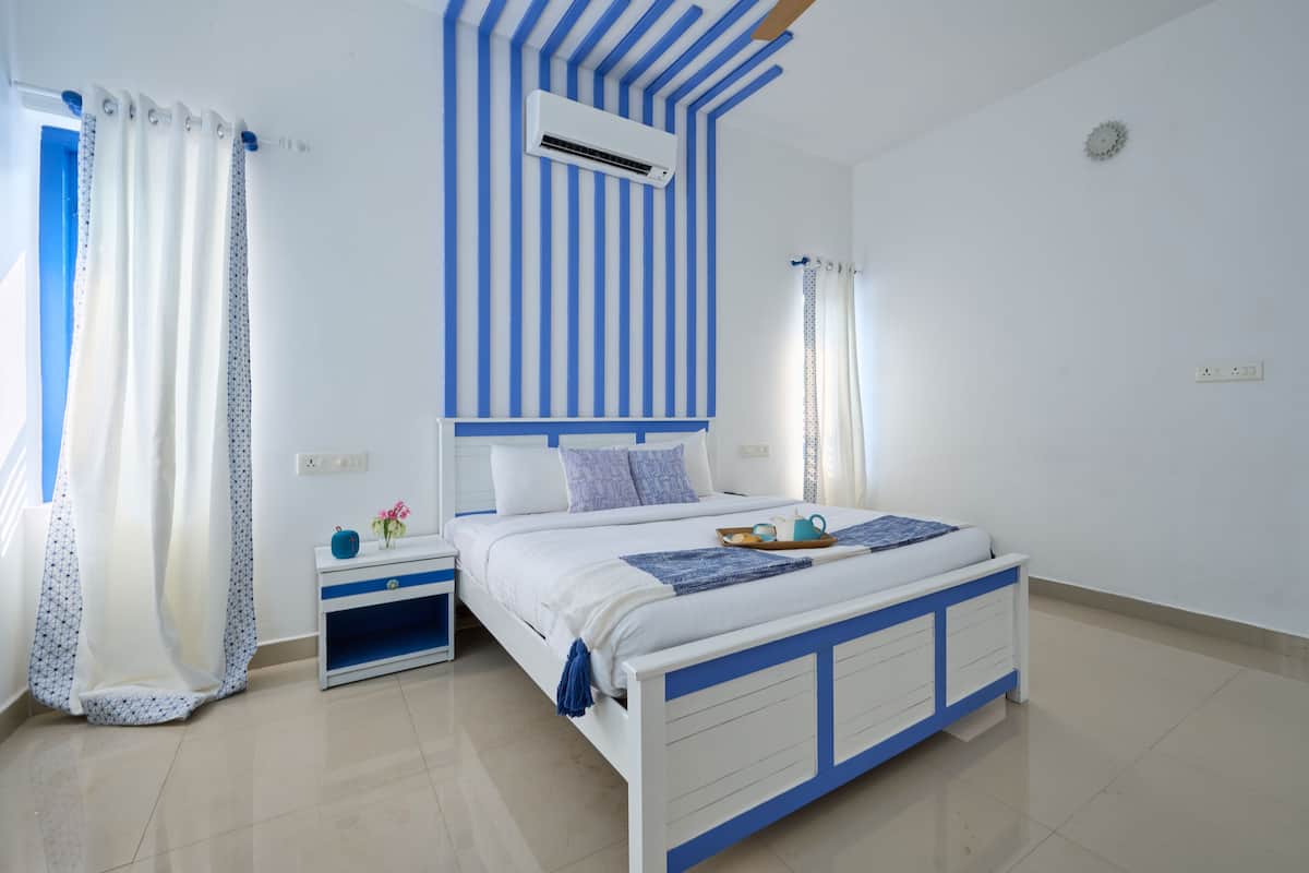 A bedroom with a bed, bedside tables, an air conditioning unit, and curtains.