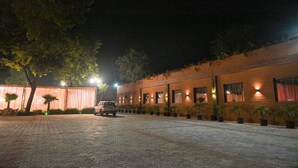 A paved courtyard with a car parked in front of a building with multiple windows and potted plants. - M D Farms & Resorts (Mathura)