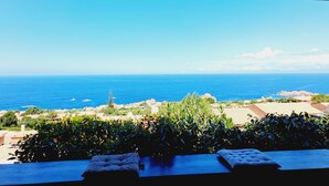 Una terraza con vista al océano, un área de estar con cojines y un muro de piedra.