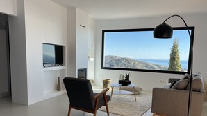 Una sala de estar moderna con un televisor grande, asientos cómodos, una chimenea y vista al mar.