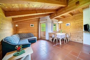 A wooden cabin interior with a sofa, dining table, and a television.