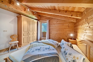 A wooden cabin bedroom with two beds, a wardrobe, a chair, and a window.