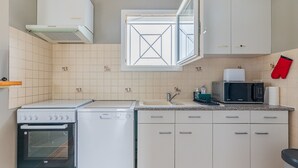 Cocina compacta con horno integrado, microondas y lavavajillas, con armarios blancos y salpicadero de azulejos.
