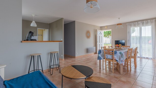 Una sala de estar moderna con sofá, una mesa de comedor con sillas, una zona de cocina con cafetera y un televisor.