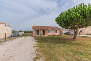 Une maison à deux étages avec une allée en gravier, un arbre dans le jardin et une voiture garée.
