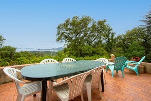 Eine Terrasse im Freien mit Tisch und Stühlen, umgeben von Grünpflanzen und Blick auf ferne Hügel.