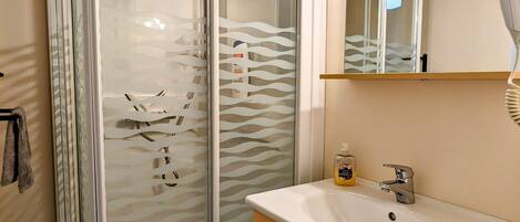 A bathroom with a glass-enclosed shower, a sink with a mirror above, and a towel rack.