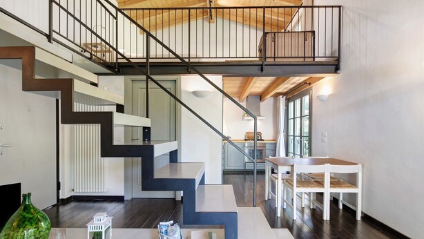 Un interior moderno con una escalera, una zona de comedor y una cocina al fondo.