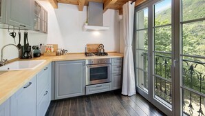 Una cocina con gabinetes grises, encimera de madera, estufa a gas y vistas a un bosque a través de amplias ventanas.