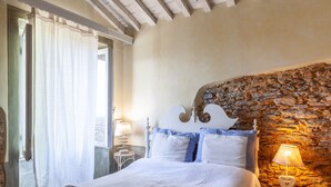 A bedroom with a stone wall, a bed with white bedding, and a nightstand with a lamp. - Holiday Home 'Il Pescino' with Private Terrace and Wi-Fi (Pietrasanta)