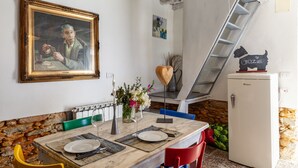 A dining area with a table set for two, a painting on the wall, a refrigerator, and a staircase. - Holiday Home 'Il Pescino' with Private Terrace and Wi-Fi (Pietrasanta)