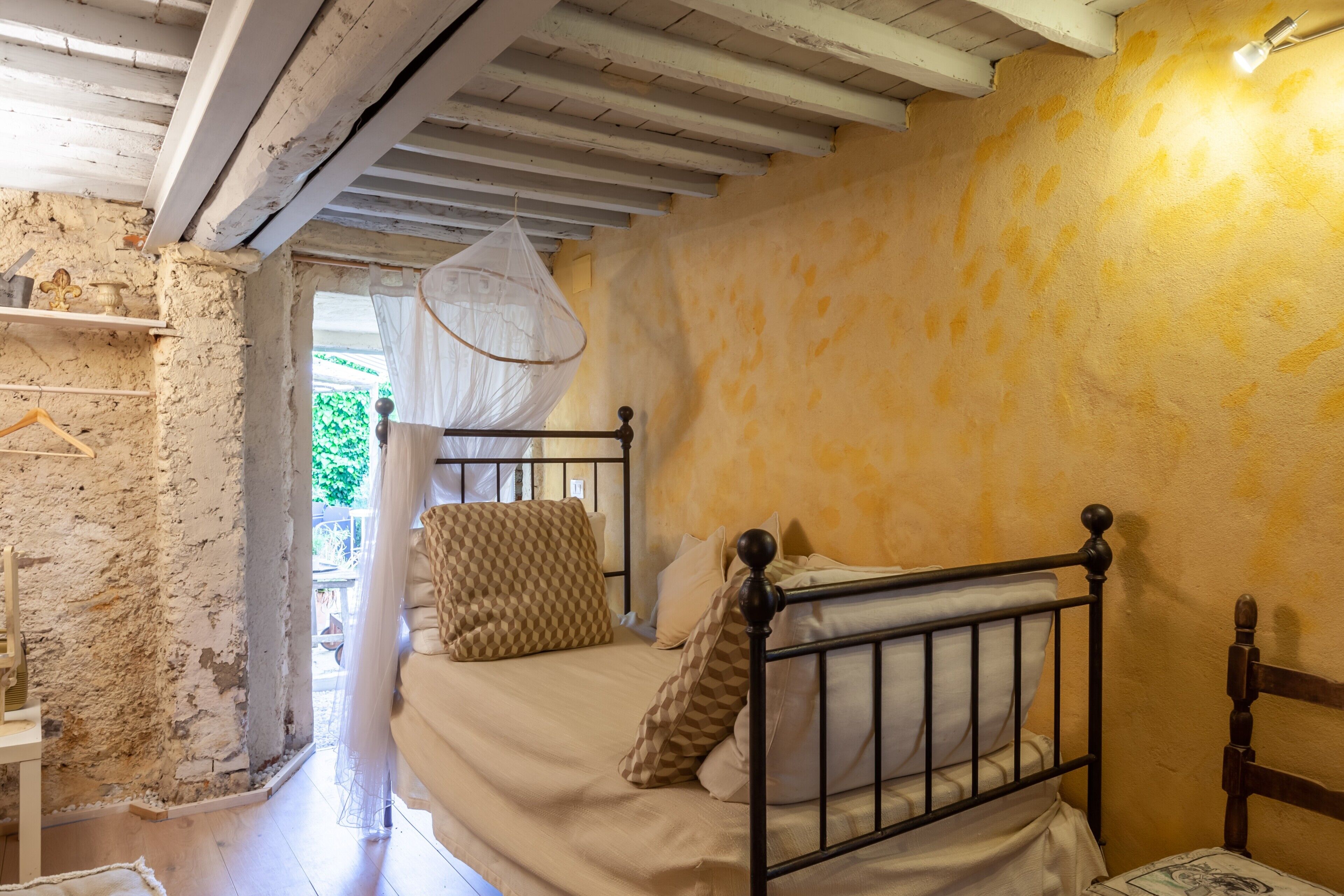 Une chambre avec un lit, une tête de lit en bois, un luminaire suspendu et une fenêtre donnant sur un paysage verdoyant.
