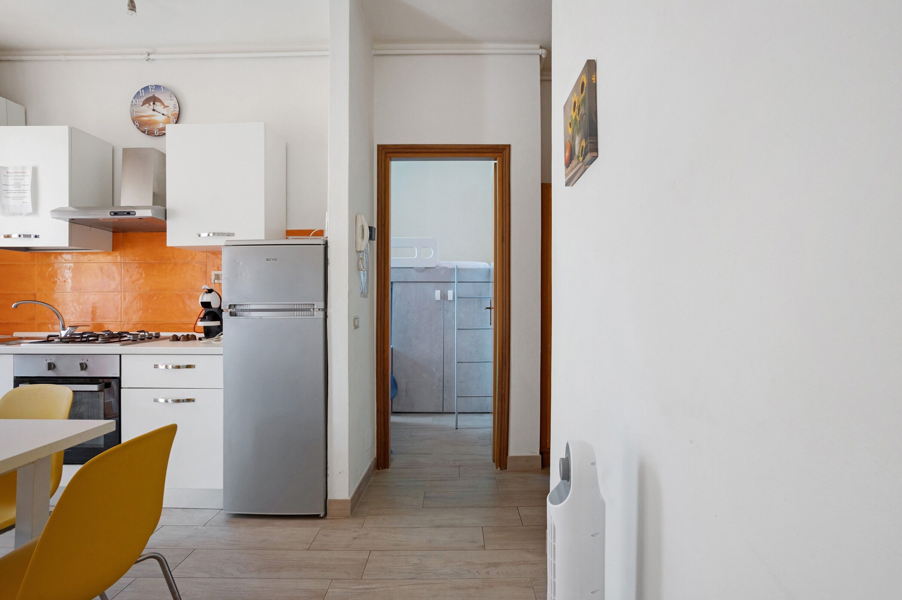 A kitchen with white cabinets, a refrigerator, a stove, and a dining area with a yellow chair.
