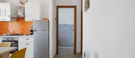 A kitchen with white cabinets, a refrigerator, a stove, and a dining area with a yellow chair.