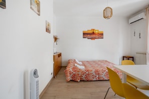 Une pièce comprenant un lit, une table, une chaise, un radiateur et des œuvres d’art accrochées au mur.