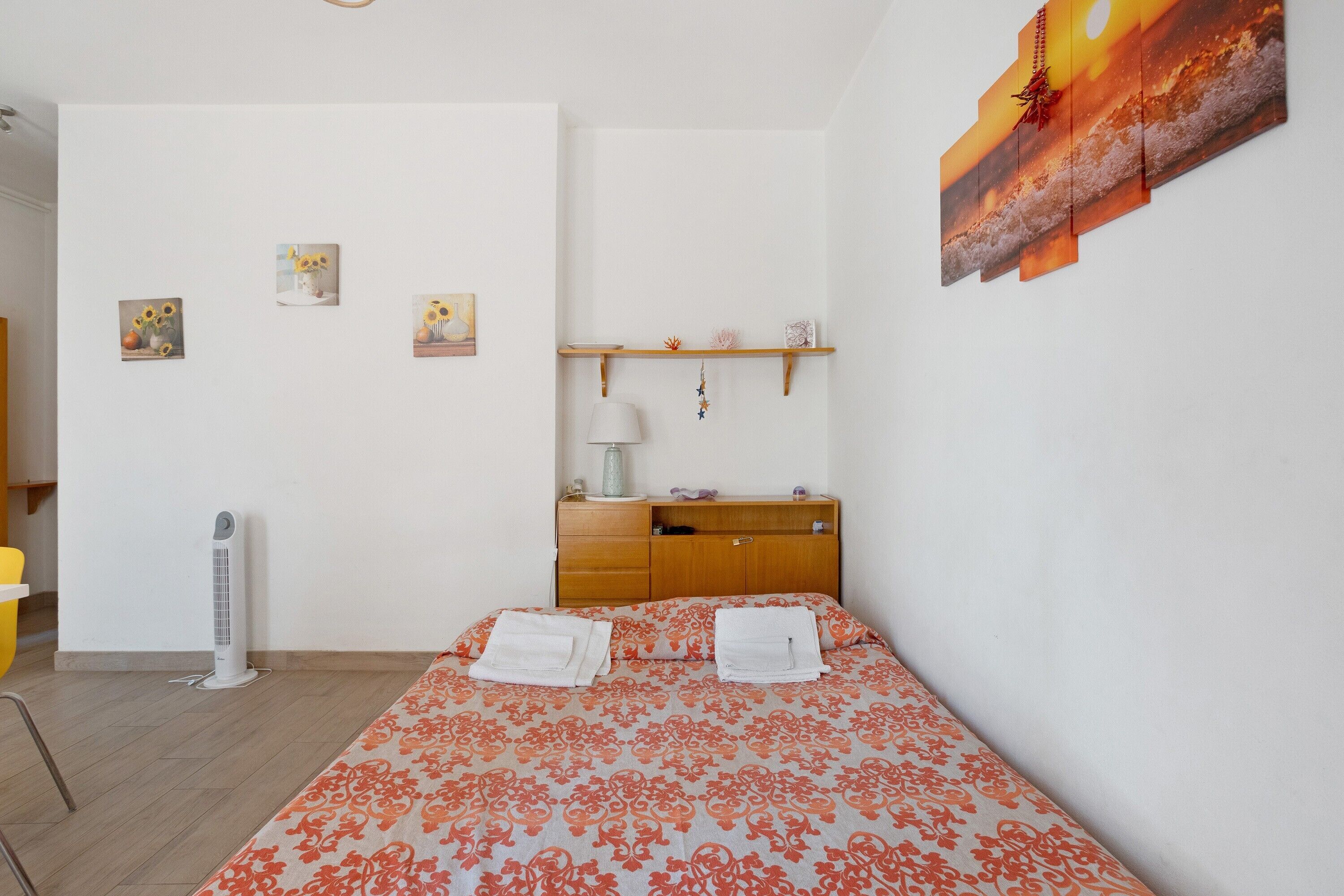 Ein Schlafzimmer mit Bett, Nachttisch, Lampe und einer Wandablage.