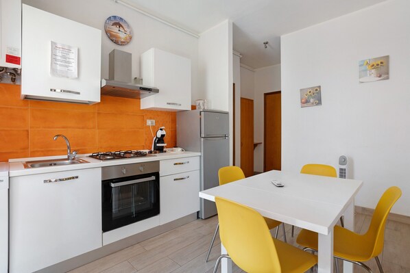 Una cocina moderna con gabinetes blancos, estufa a gas y horno empotrado. Cuenta con un comedor con mesa blanca y sillas amarillas.
