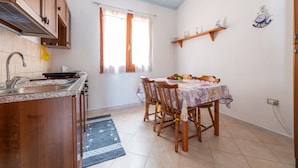 A kitchen with wooden cabinets, a sink, and a dining area with a table set for two. - Vacation Home "Villa Leonardo Sud Sardegna" with Sea View, Private Terrace & Wi-Fi (Chia)