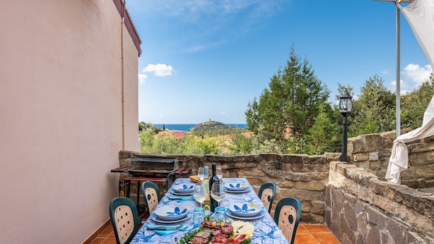 A table set for dining with a view of the sea and hills. - Vacation Home "Villa Leonardo Sud Sardegna" with Sea View, Private Terrace & Wi-Fi (Chia)