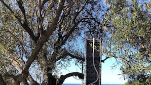 A cylindrical structure with a textured surface, possibly a water feature or sculpture, surrounded by trees and a clear sky. - Vacation Home "Villa Leonardo Sud Sardegna" with Sea View, Private Terrace & Wi-Fi (Chia)